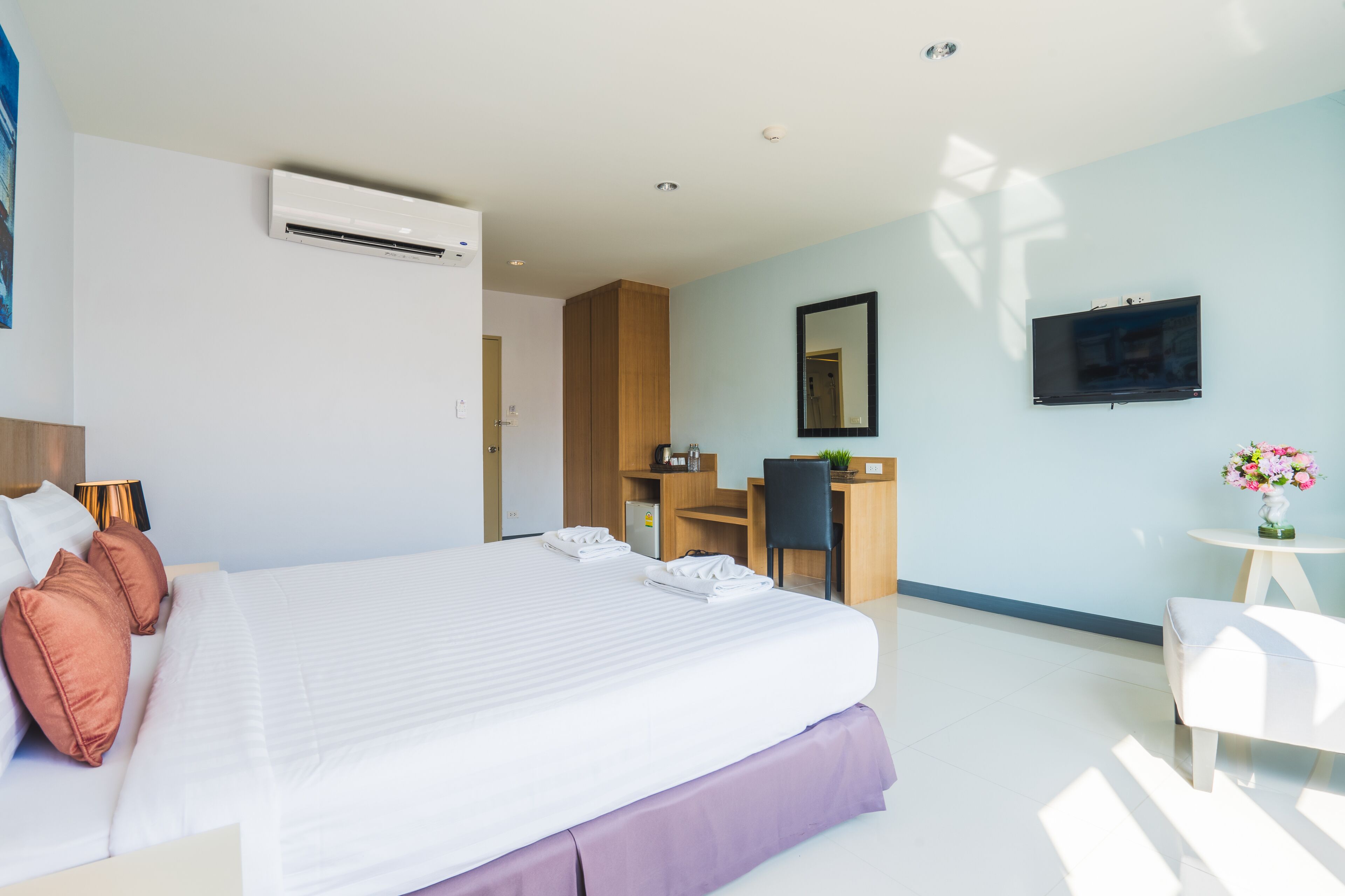 A modern hotel room with a large bed, a desk, a chair, a TV, and an air conditioning unit.