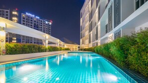 A swimming pool with tiled edges, surrounded by greenery and adjacent to a building with signage. - Vapa Hotel (Phuket)
