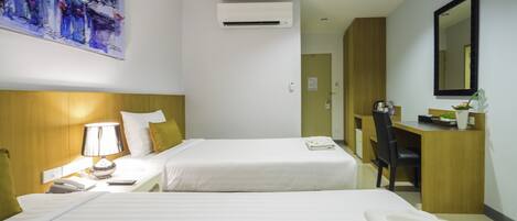 A hotel room with two beds, a desk, a chair, a lamp, an air conditioner, and a painting on the wall.