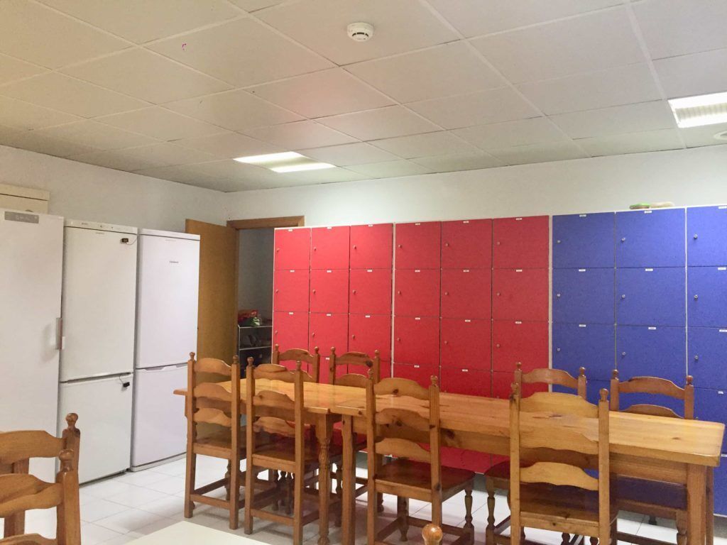 Um quarto com uma mesa e cadeiras de madeira, um refrigerador branco e armários em vermelho e azul.