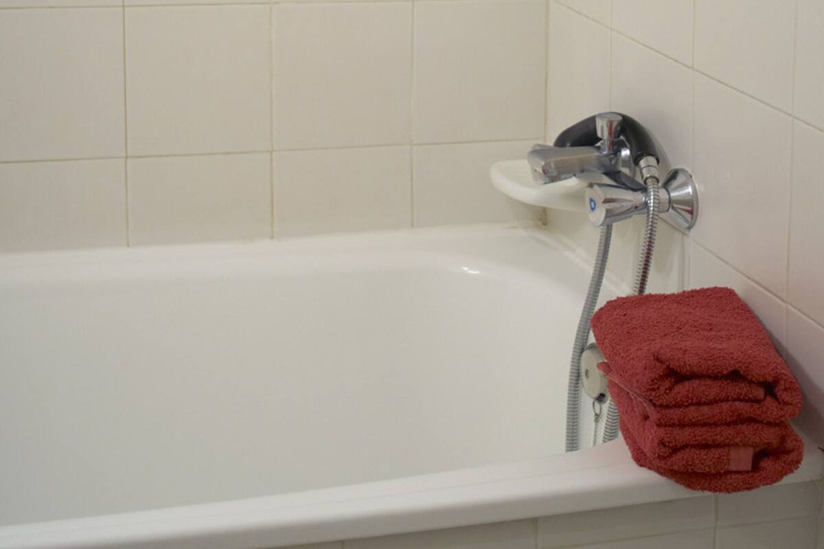 A white bathtub with a showerhead, a red towel, and a white tiled wall.