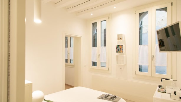 A hotel room with a bed, a TV, a desk with a mirror, and a window with curtains. - San Marco Design Suites (Venice)