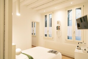 A hotel room with a bed, a TV, a desk with a mirror, and a window with curtains. - San Marco Design Suites (Venice)