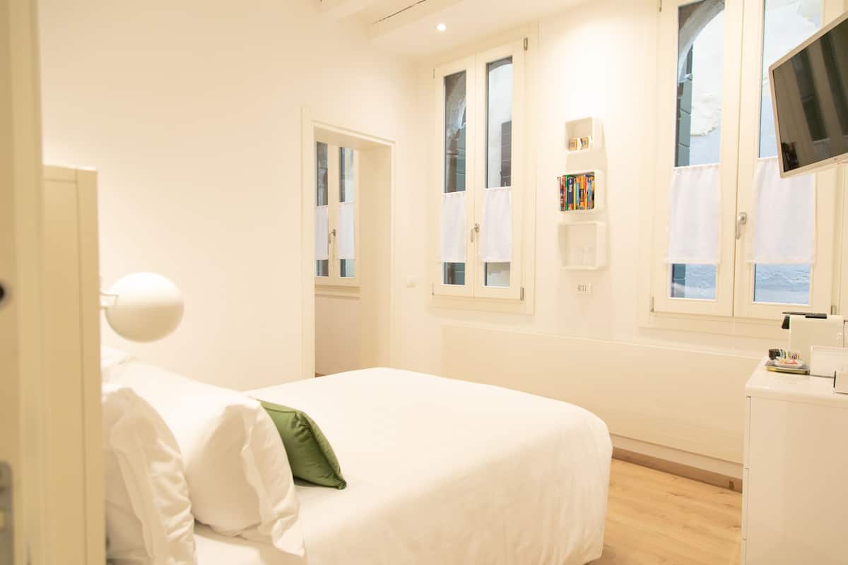 A hotel room with a bed, a desk, a chair, a TV, and a window with curtains.