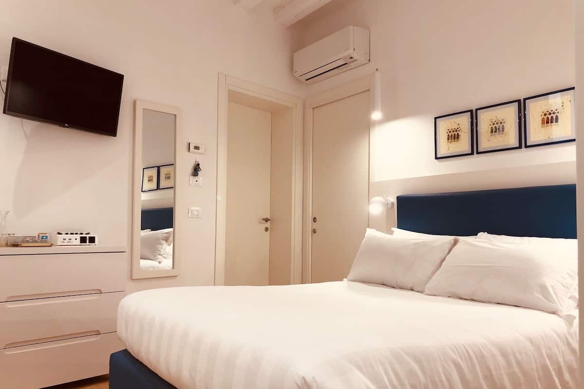 A bedroom with a bed, a TV, a wardrobe, and a mirror.