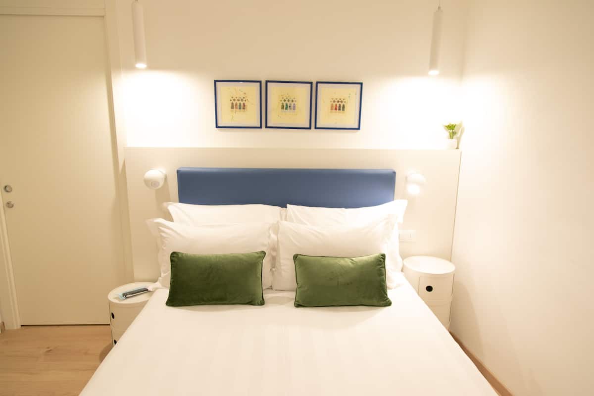 A neatly made bed with white and green pillows, a blue headboard, and three framed pictures on the wall.