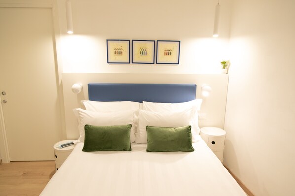 A neatly made bed with white and green pillows, a blue headboard, and three framed pictures on the wall. - San Marco Design Suites (Venice)