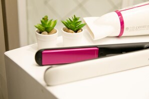 A white table with a pink and black hair straightener, two small potted plants, and a rolled-up white object with a pink band. - San Marco Design Suites (Venice)