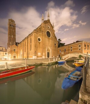 A historic building with a prominent tower and arched windows, situated by a calm waterway with boats. - San Marco Design Suites (Venice)
