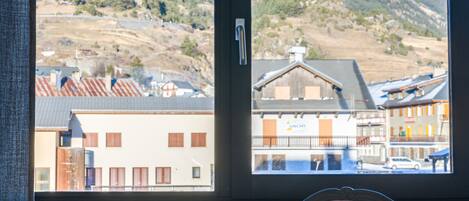 A room with a large window offering a view of a mountain and a village.