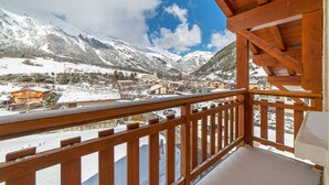 Un balcon en bois donnant sur un village de montagne enneigé, avec des bâtiments et un ciel dégagé.