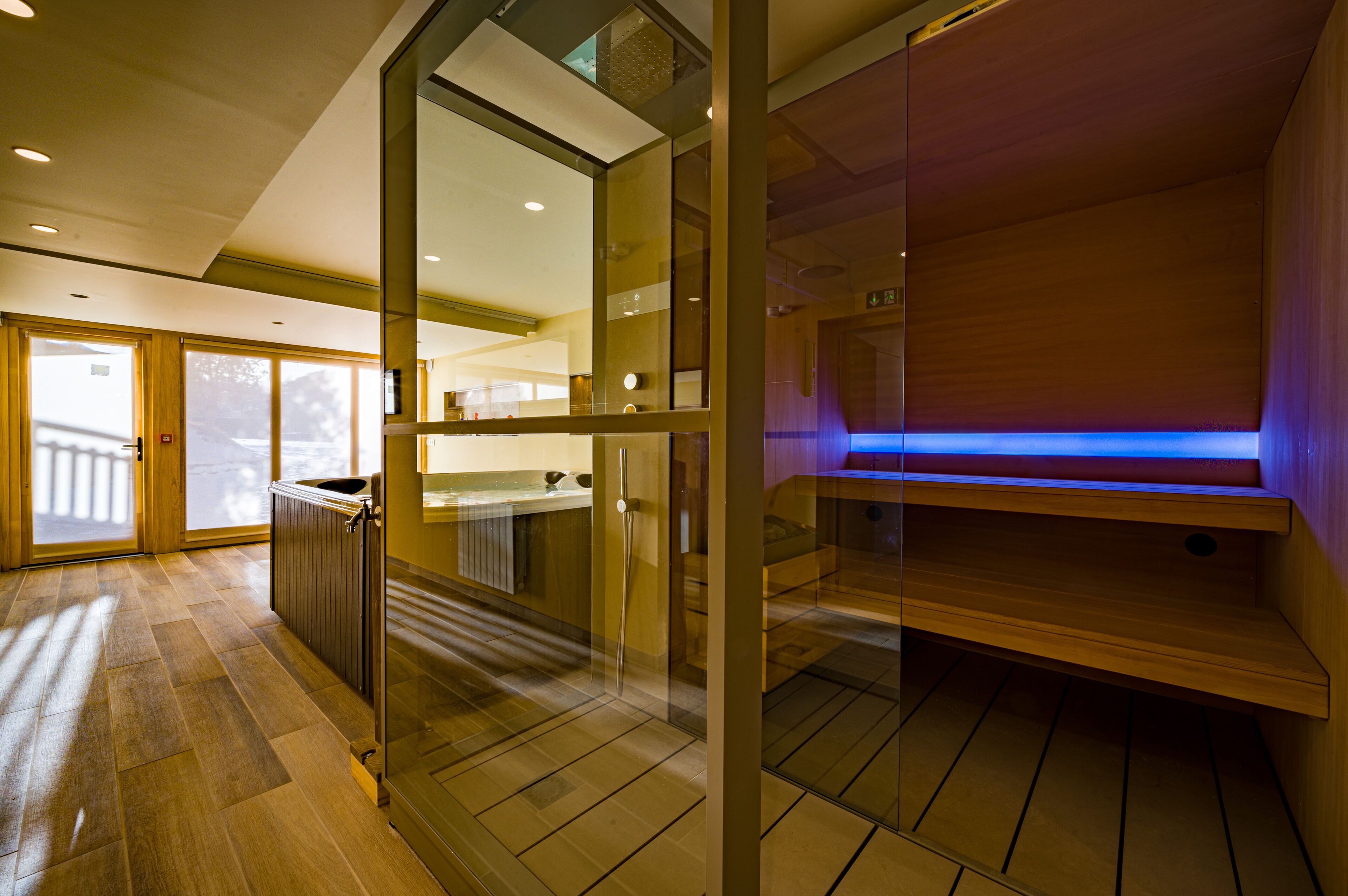 Un interno moderno con una parete divisoria in vetro, pavimento in legno e un'area illuminata di blu.