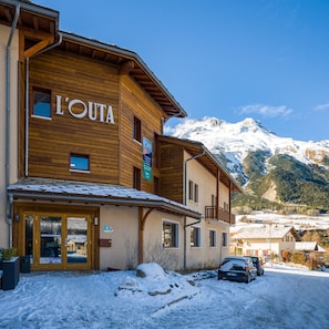 A wooden building with a sign reading "L'OUTA" and a view of snow-covered mountains in the background.