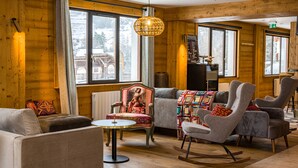 L’intérieur chaleureux d’un chalet en bois, avec des murs en bois, de grandes fenêtres et un assortiment de sièges comprenant un canapé, des fauteuils et un fauteuil à bascule.