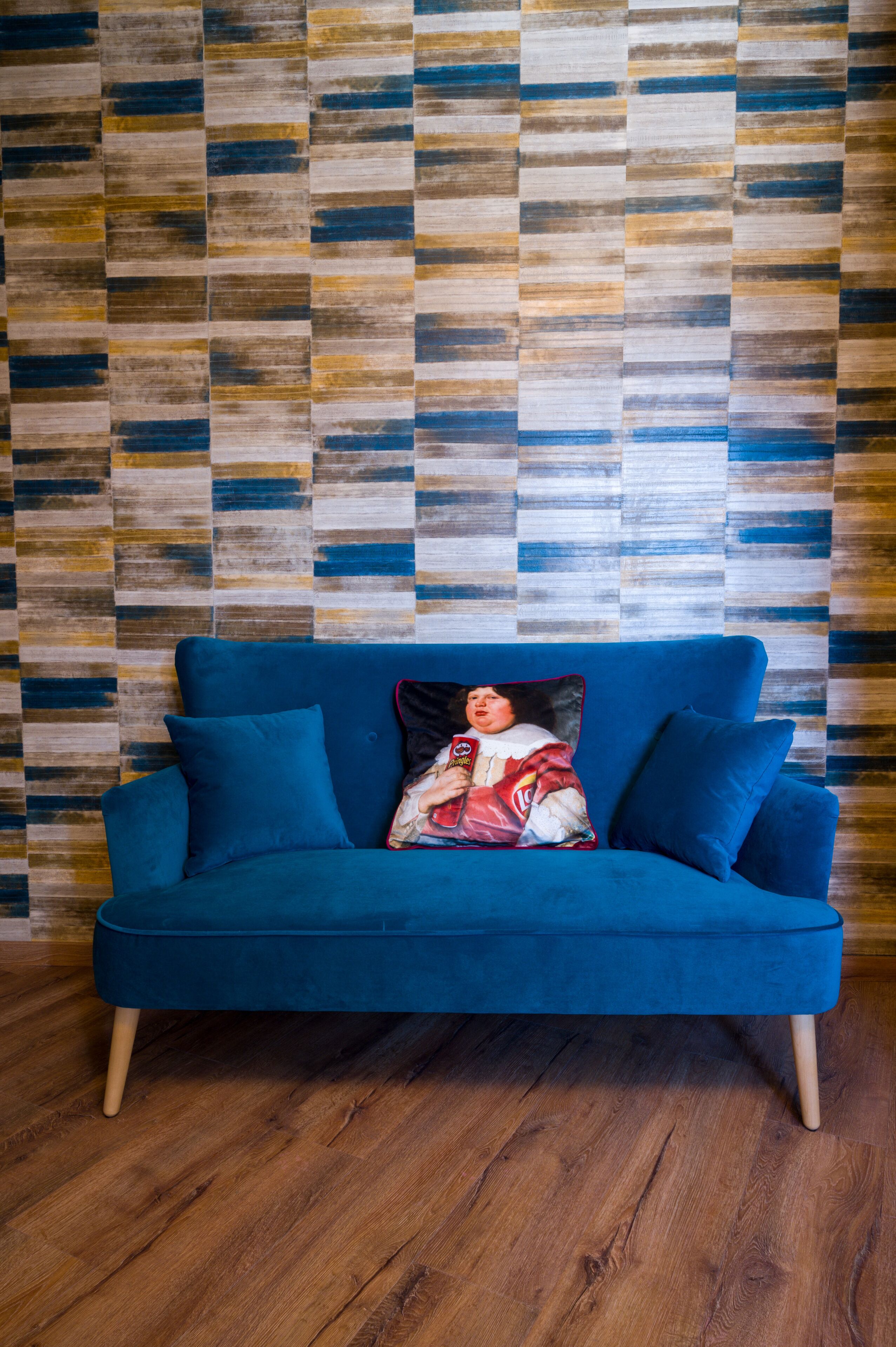 A blue sofa with wooden legs against a wooden-patterned wall.