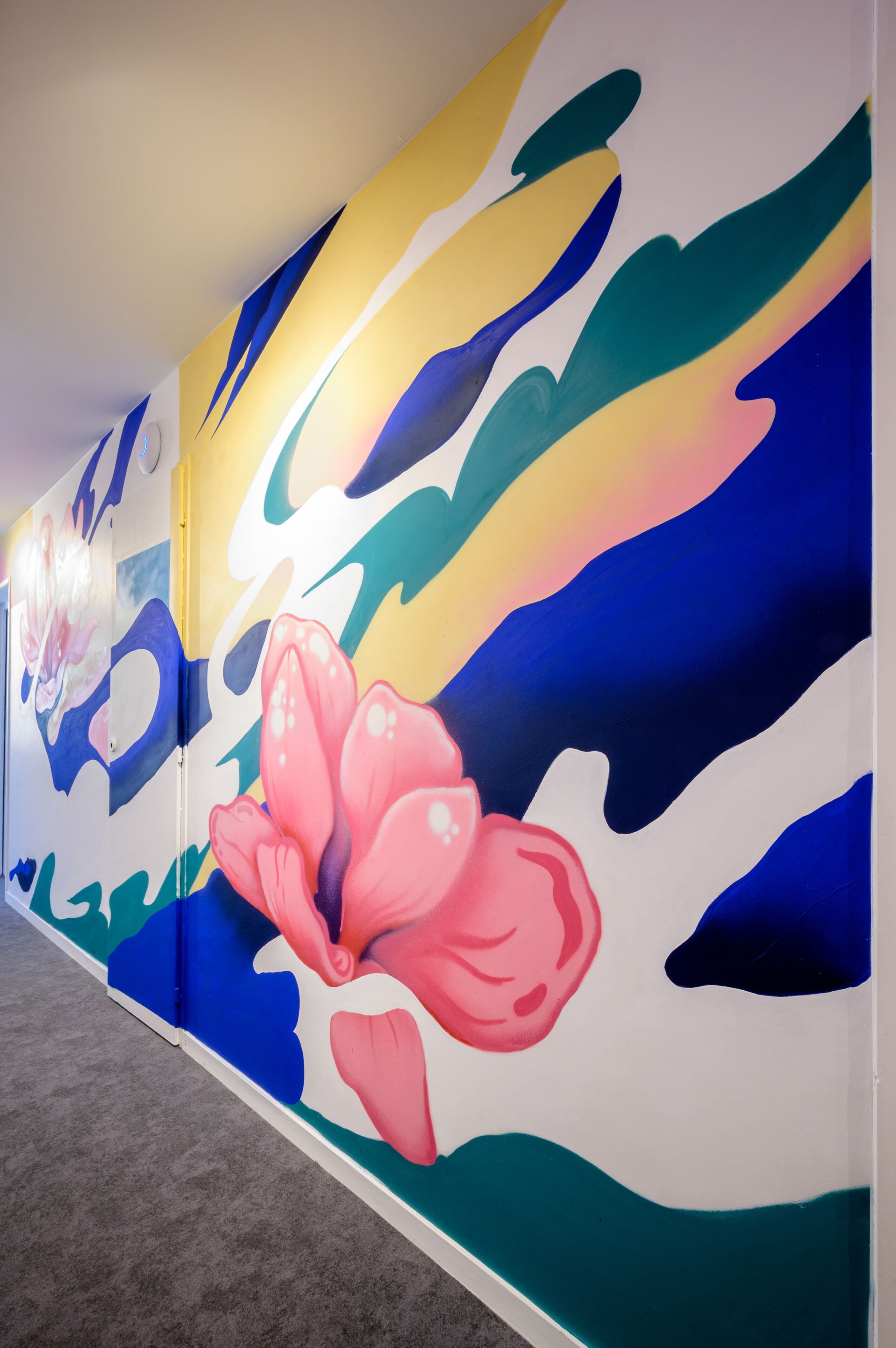 Un pasillo con llamativas obras de arte abstracto en la pared, destacando una flor rosa prominente.