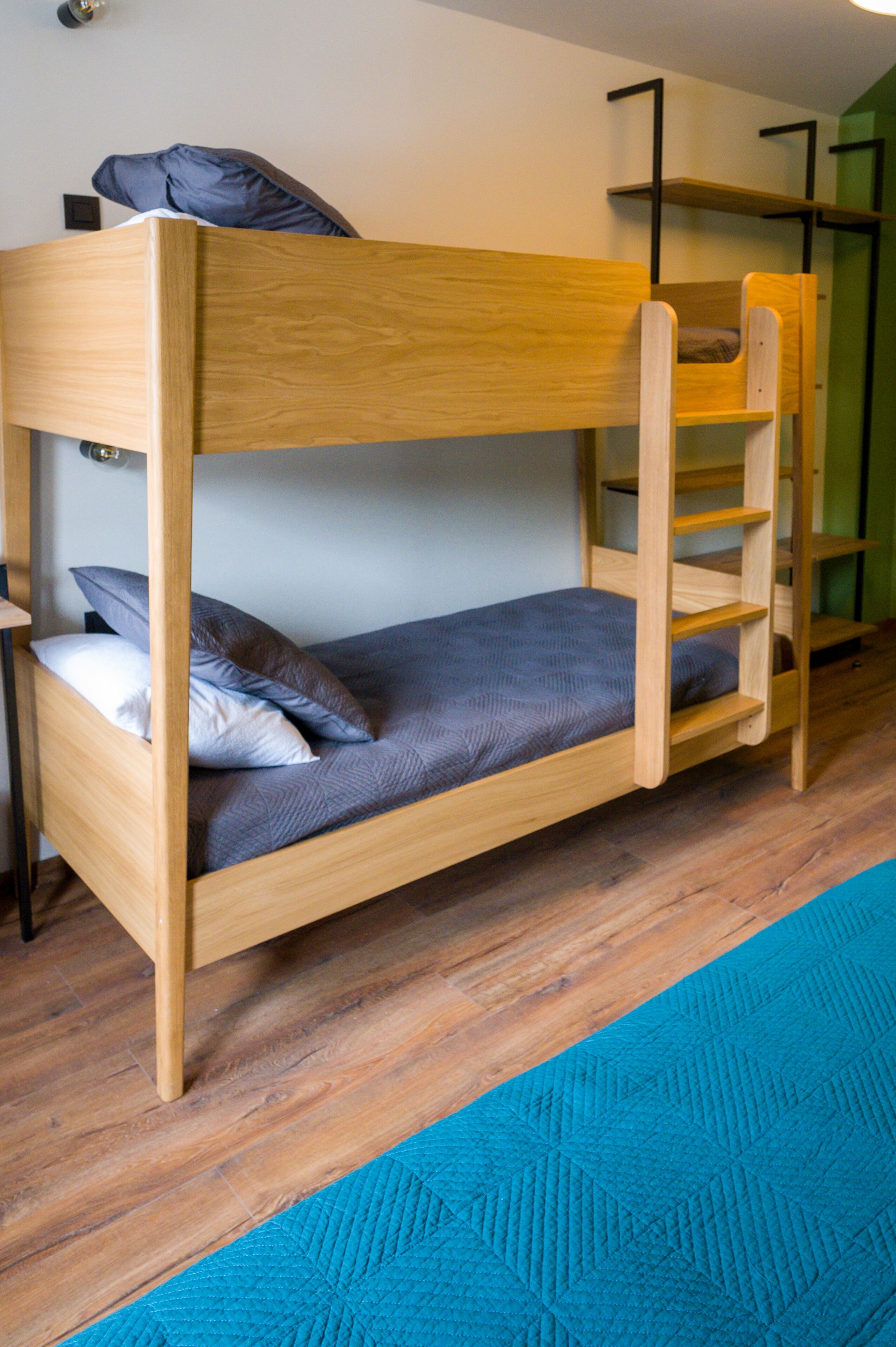 Una cama litera con estructura de madera, colchón azul y una escalera.