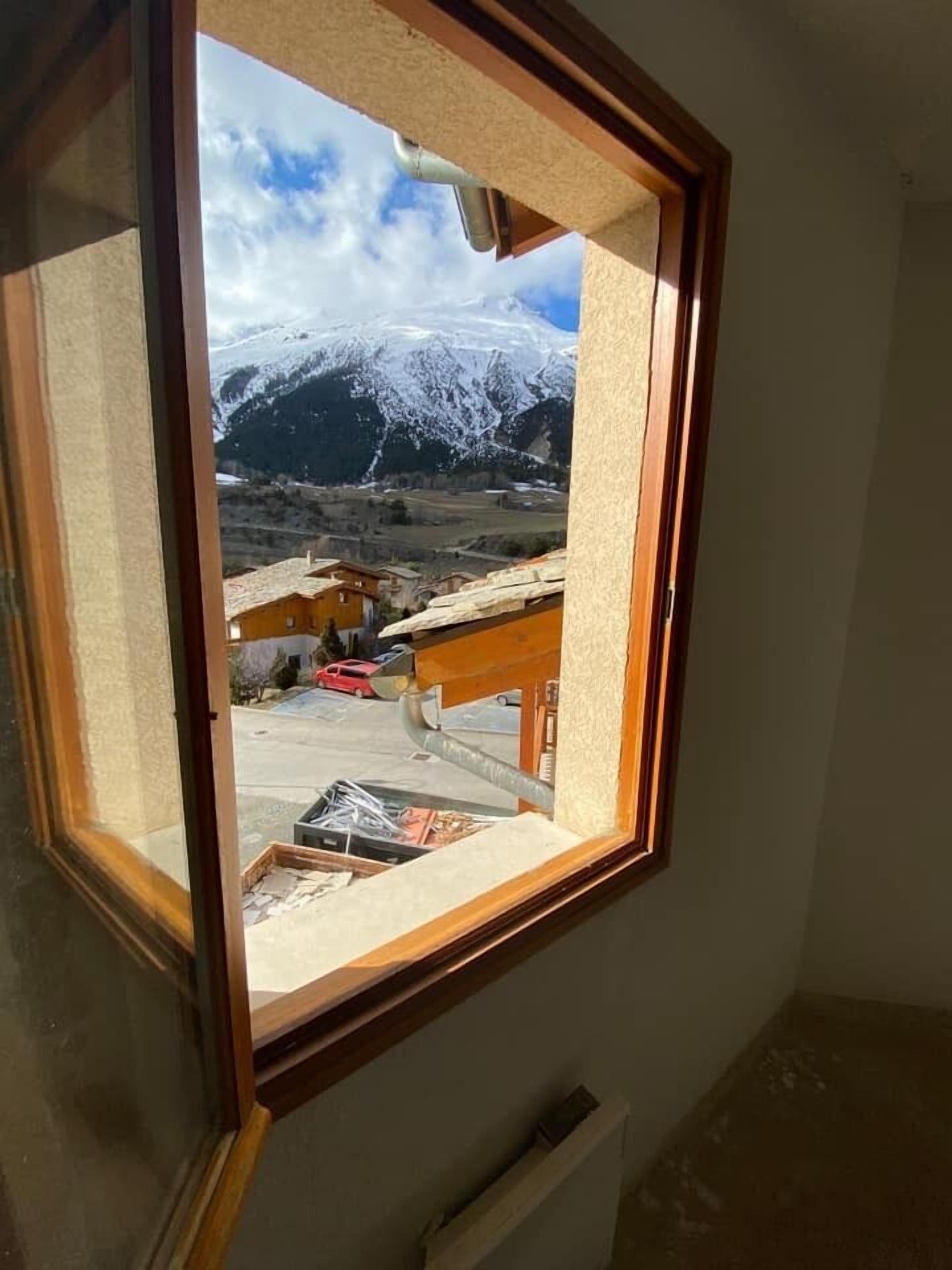 Een kamer met een raam dat uitkijkt op een besneeuwde berg en een klein dorp.