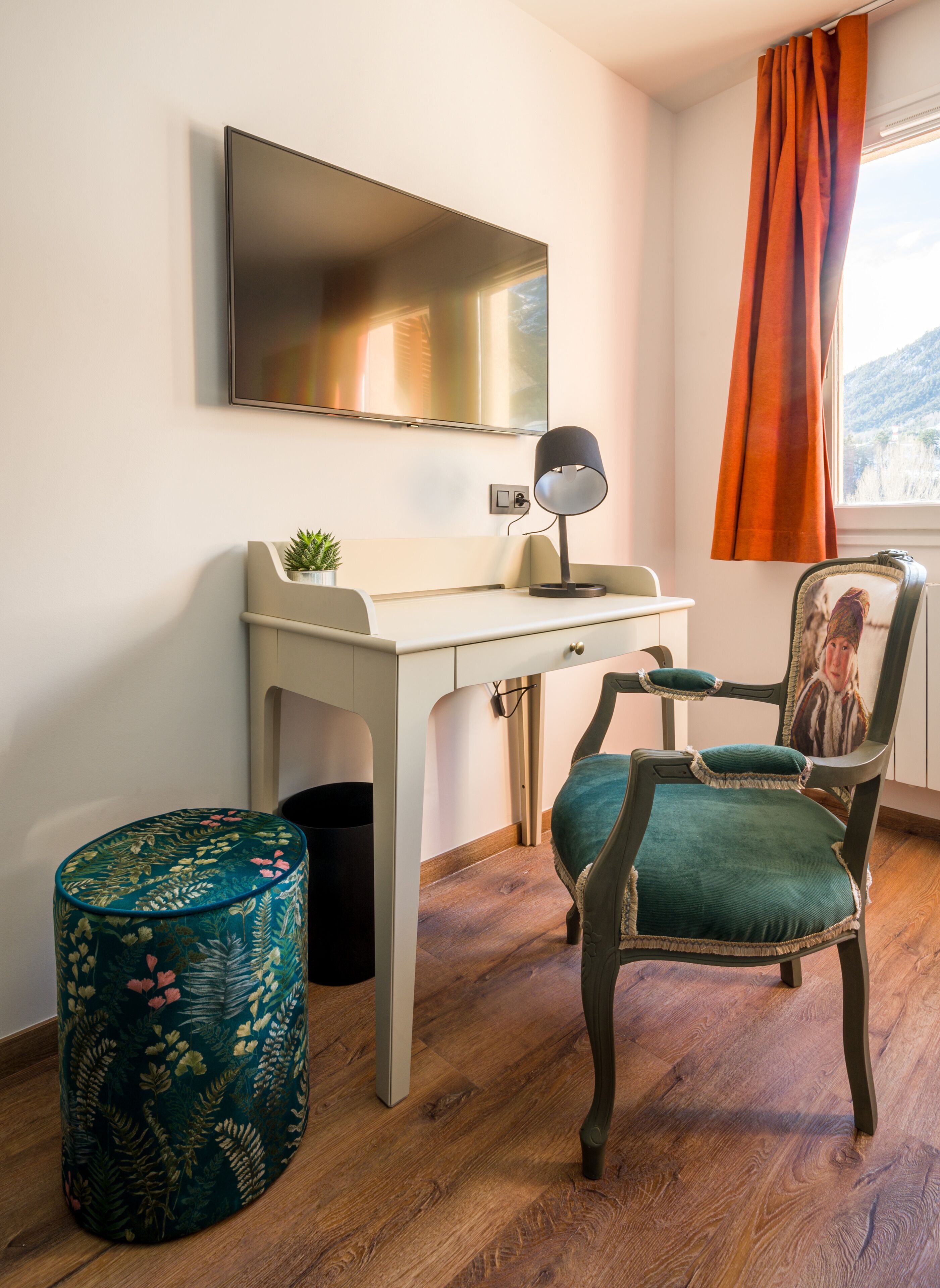 A room with a desk, a chair, a small plant, and a television mounted on the wall.