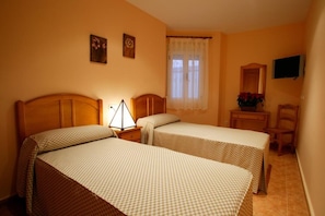 A bedroom with two beds, a nightstand with a lamp, a chair, a TV, and a window with curtains.