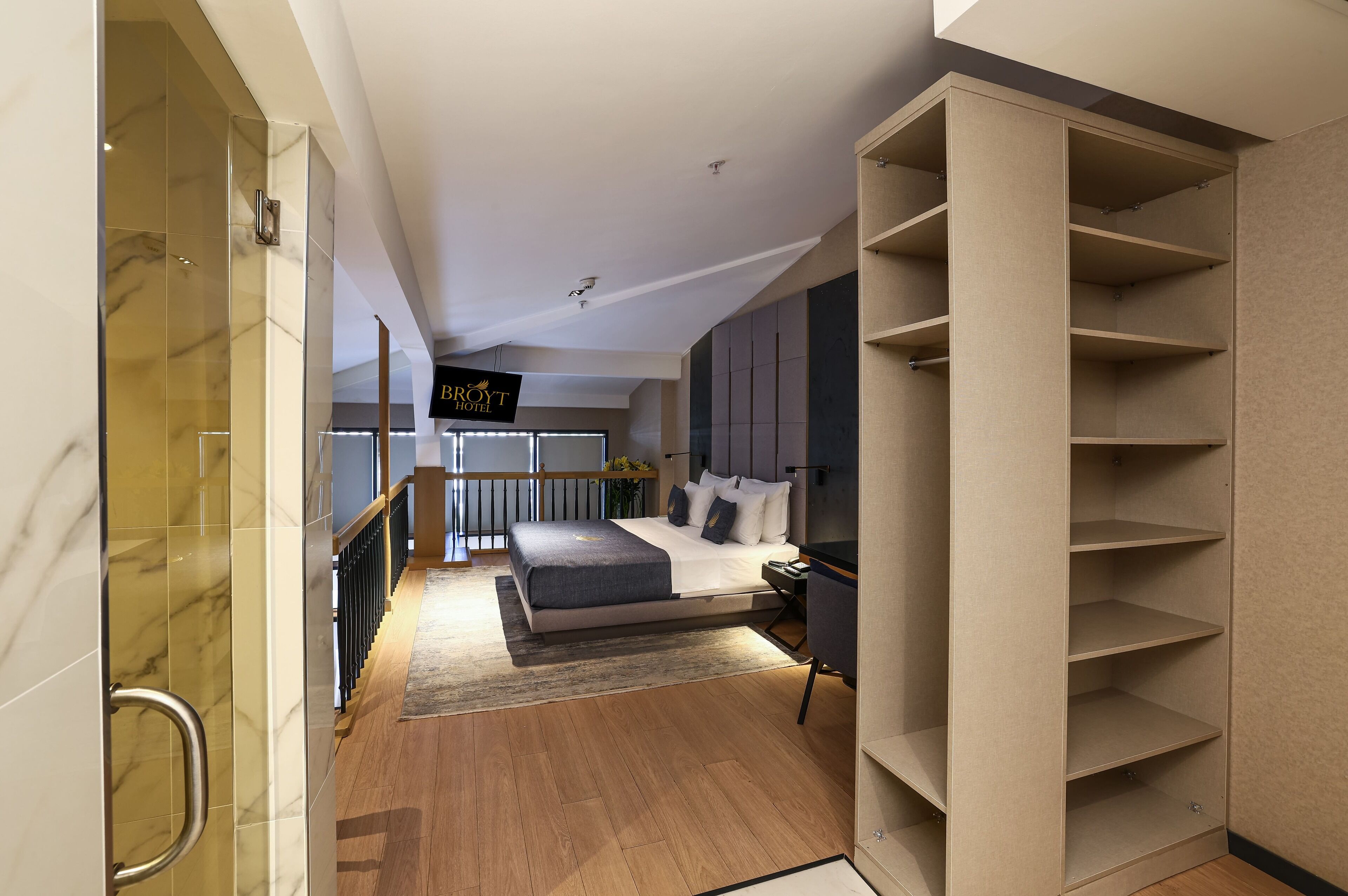 A modern hotel room with a large bed, built-in shelving, and a glass shower enclosure.