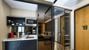 A modern kitchen with a built-in microwave, a coffee maker, and a kettle. There is a sliding door leading to a bedroom with a bed and a wardrobe. - Broyt Hotel (Istanbul)
