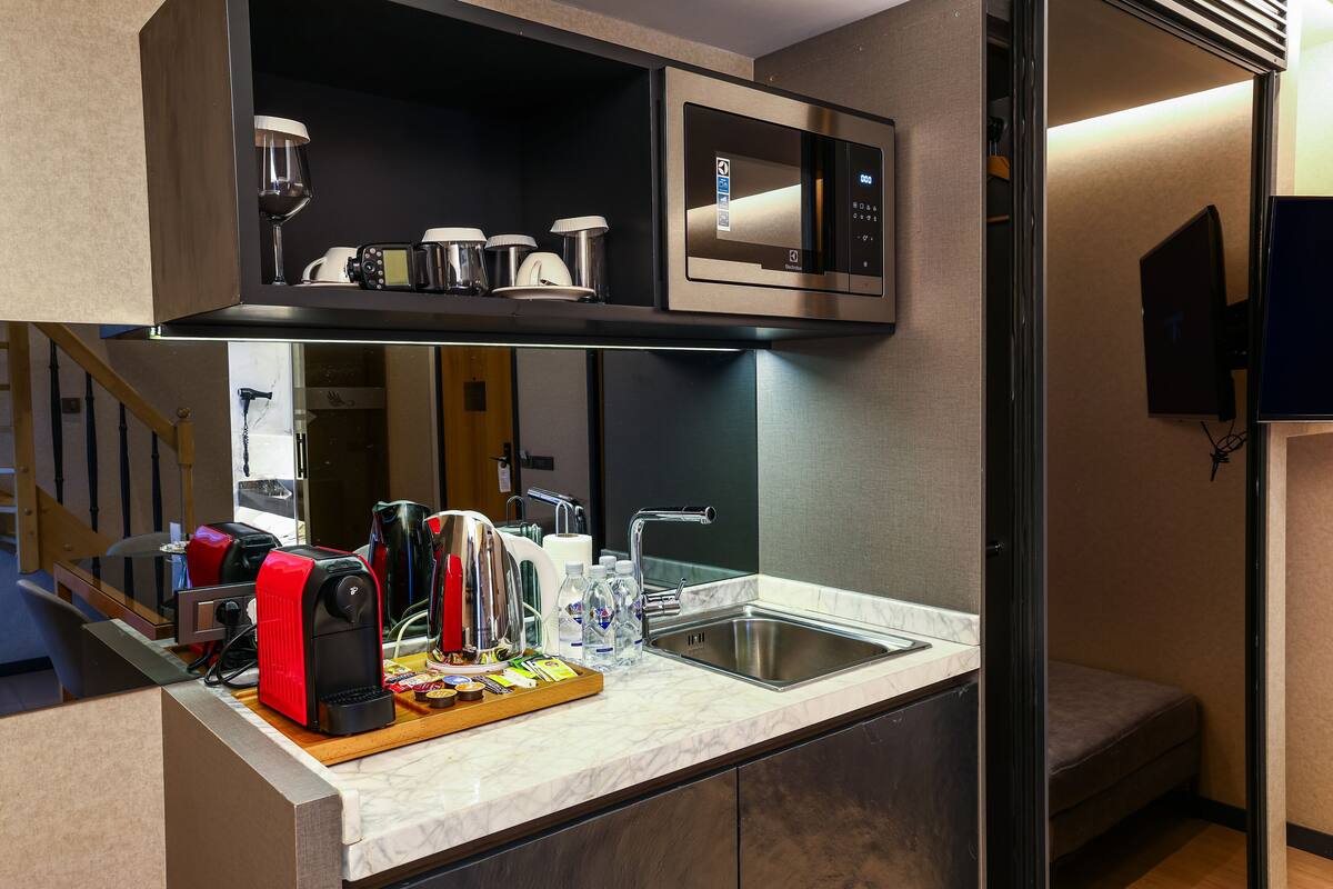 A modern kitchen with a built-in microwave, coffee maker, and kettle. There is a sink and a countertop with a tray of breakfast items.
