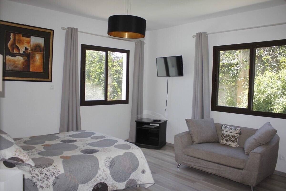 Een slaapkamer met een bed, een bank, een televisie en grote ramen.