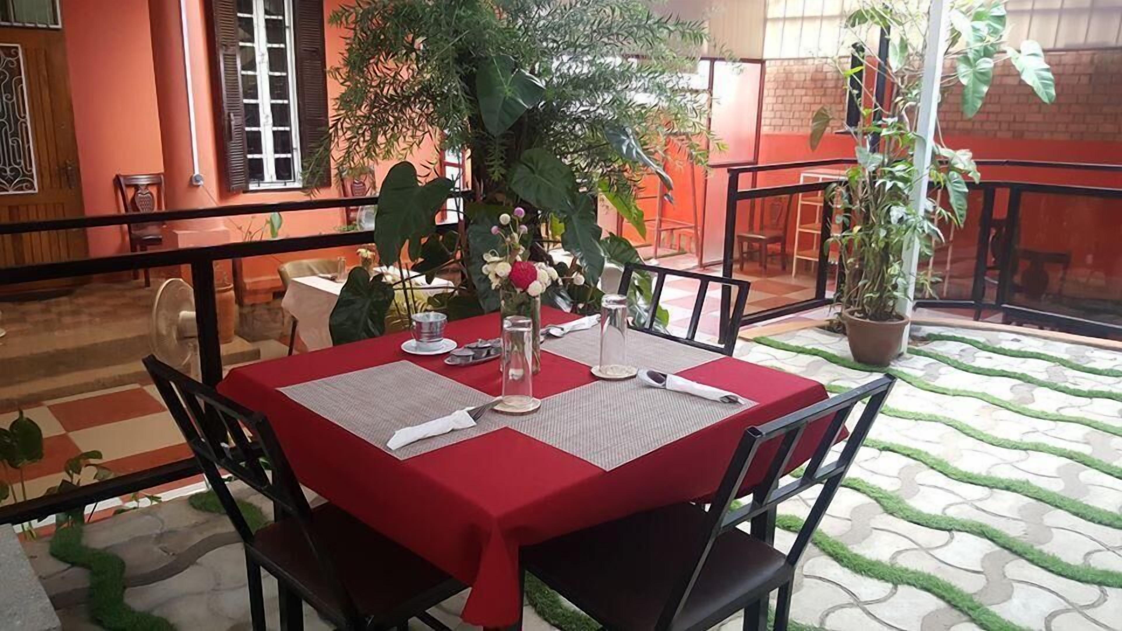 Un área de comedor al aire libre con mantel rojo, sillas negras y una planta en maceta.