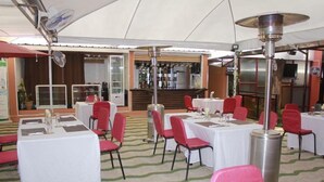 Un comedor interior con mesas y sillas, una barra al fondo y un ventilador de techo.