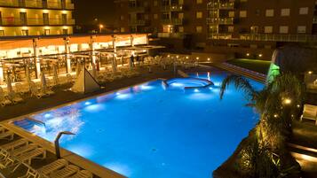 A swimming pool with lounge chairs and a bar area, surrounded by a building with multiple balconies.
