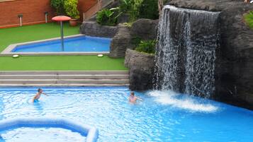 Relax by the pool with a waterfall feature, surrounded by lush greenery and a brick wall.