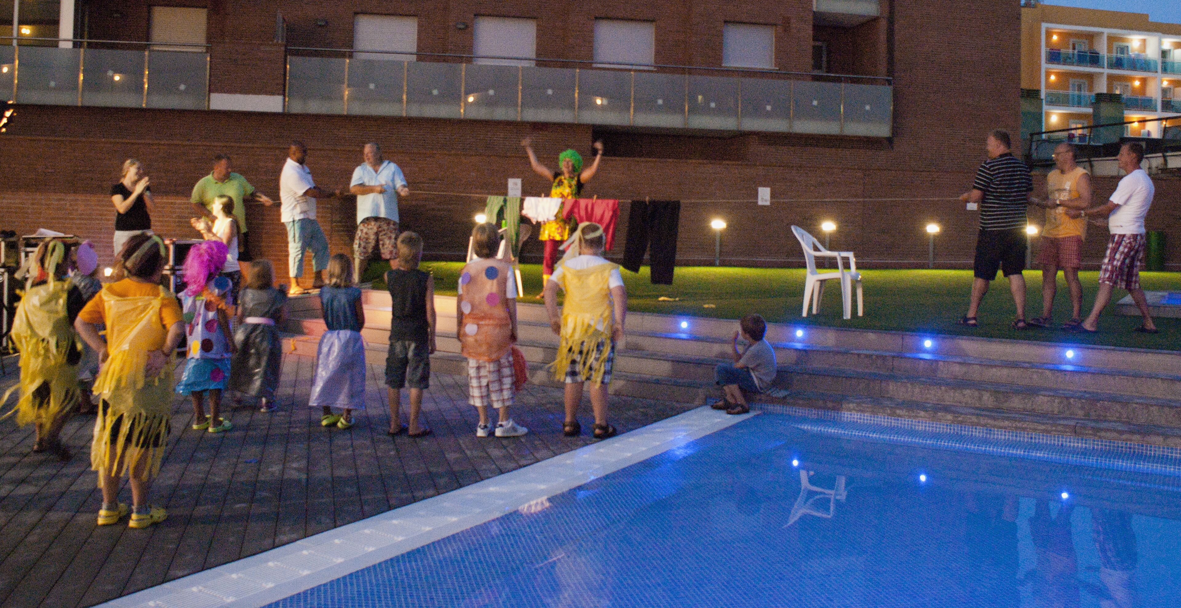 A group of people around a pool with a brick building in the background.