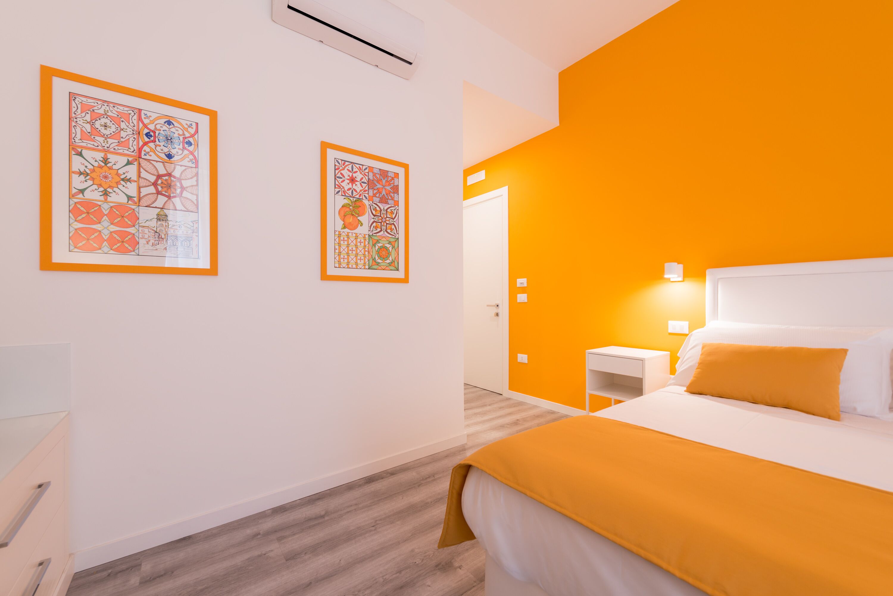 Quarto de hotel com uma cama, uma mesinha de cabeceira e duas obras de arte emolduradas na parede.