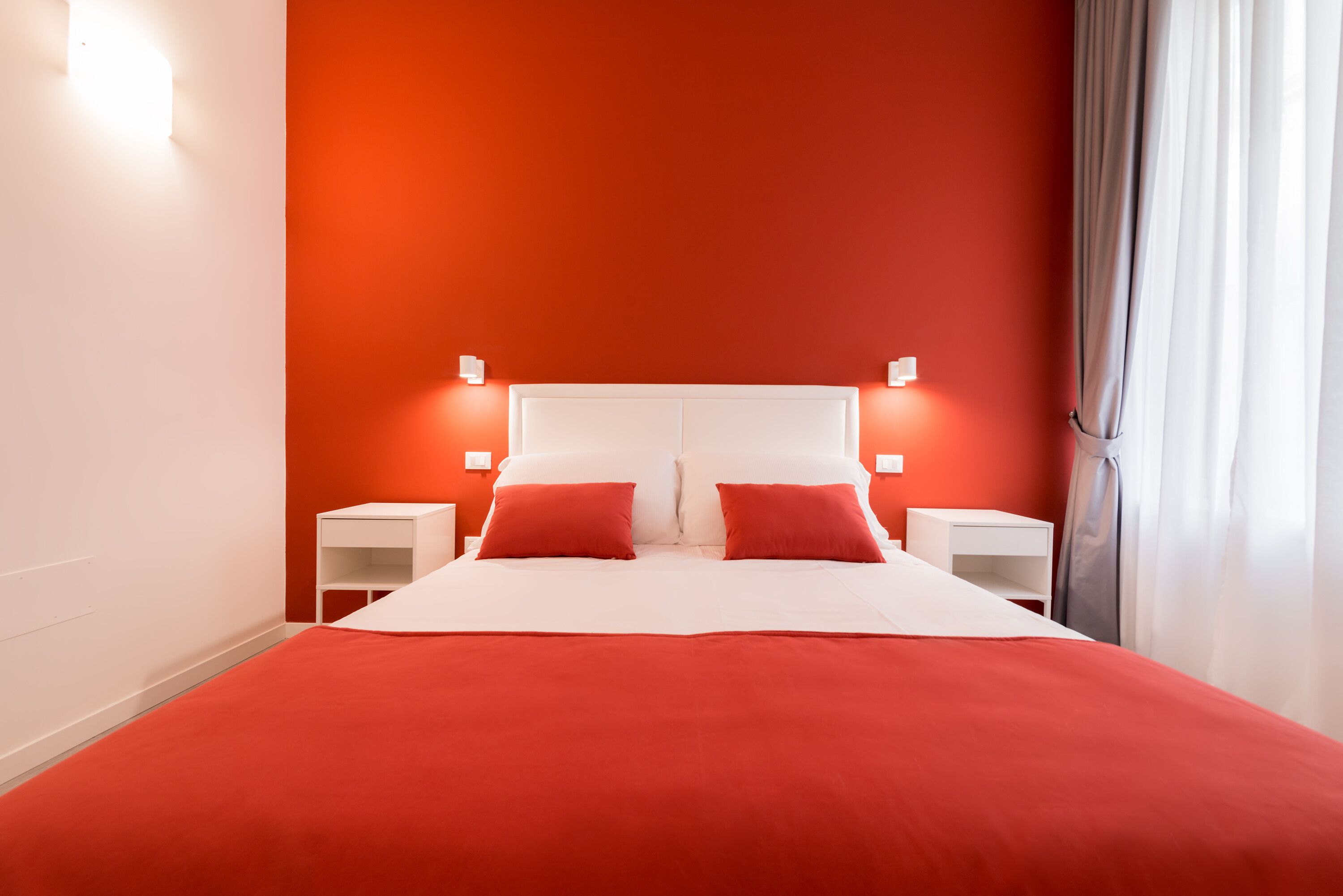 Un lit avec une couvre-lit rouge et des oreillers, une tête de lit blanche et deux tables de chevet avec des lampes.