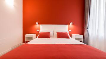 Un lit avec une couvre-lit rouge et des oreillers, une tête de lit blanche et deux tables de chevet avec des lampes.