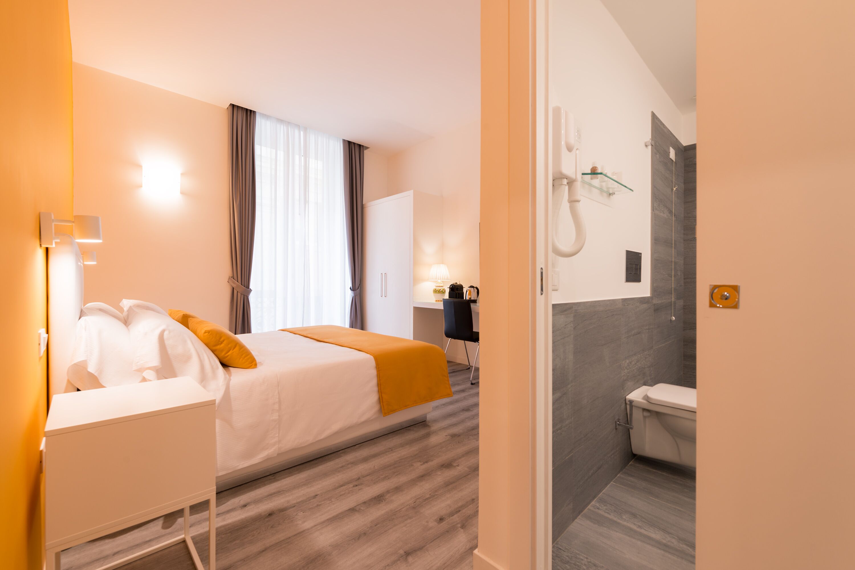 Ett hotellrum med en säng, ett skrivbord, en stol, ett badrum och en dusch.
