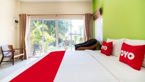 Habitación de hotel con una cama, dos almohadas rojas, un banco y vistas a zonas verdes.