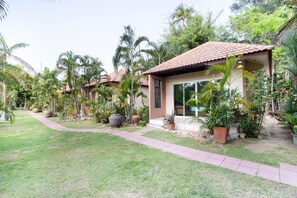 A residential property with a tiled roof, a paved pathway, and lush greenery including palm trees and potted plants. - OYO Kanum Kanoon Resort (Bang Lamung)