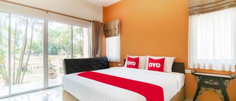 A bedroom with a large bed, a small table, and a view of greenery outside.