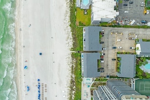 An aerial view of a coastal hotel with a beach, parking area, and multiple buildings.