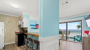 Une cuisine équipée d’un réfrigérateur, d’un four à micro-ondes et de tabourets de bar. Une fenêtre offre une vue sur la plage et sur un autobus rouge.