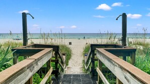 Un sentier en bois qui mène à une plage, avec un ciel dégagé.