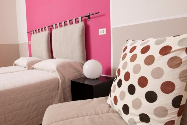 Une chambre d’hôtel avec deux lits, un mur d’accent rose et un coussin à pois.