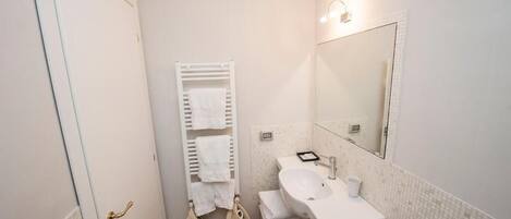 Un baño pequeño y limpio con un lavamanos blanco, un espejo y un perchero para toallas.