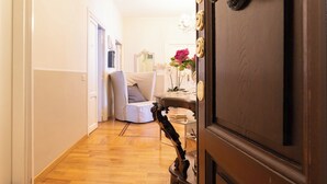 A hallway with a wooden floor, a white door with a brass handle, a white chair, and a small table with a vase of flowers. - Florian Rooms  (Rome)
