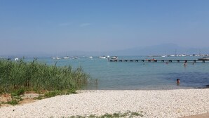 A pebbled beach with boats and a pier extending into calm waters. - Casa Linda (Lazise)