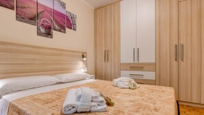 A hotel room with a large bed, wooden wardrobe, and artwork on the wall. - Garden Residence Malcesine Lake View (Malcesine)