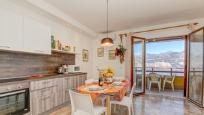 A modern kitchen with white cabinets, a built-in oven, and a dining area with a table set for four. - Garden Residence Malcesine Lake View (Malcesine)