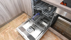 An open dishwasher with racks and a control panel, located in a kitchen with a tiled floor and wooden cabinets. - Garden Residence Malcesine Lake View (Malcesine)
